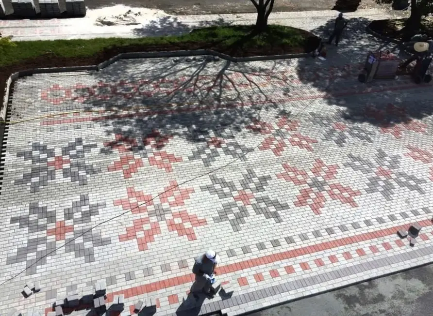 Praça pavimentada com pavers cinza, grafite e vermelhos formando desenhos de flores.