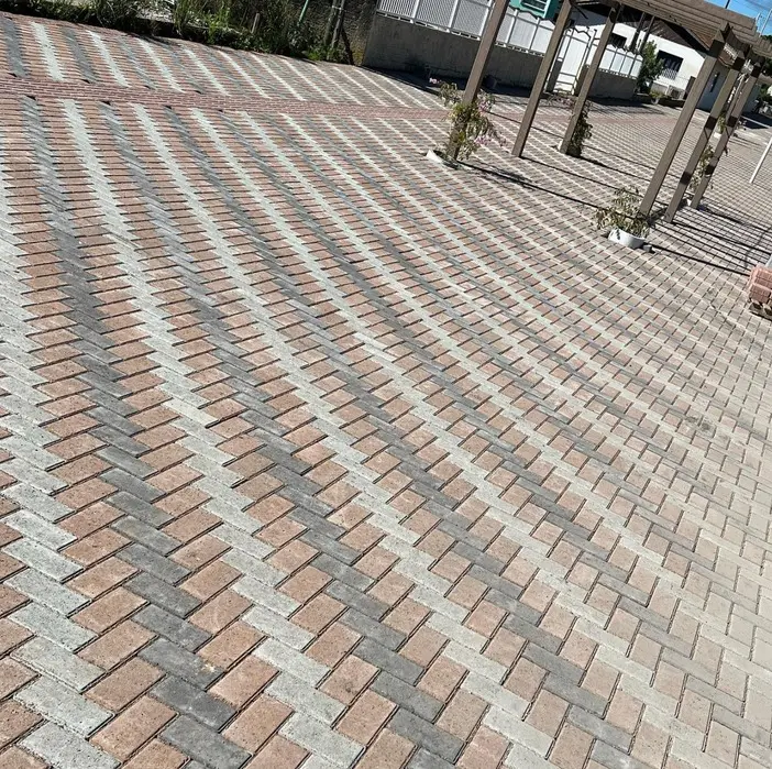 Área externa pavimentada com pavers coloridos em espinha de peixe.